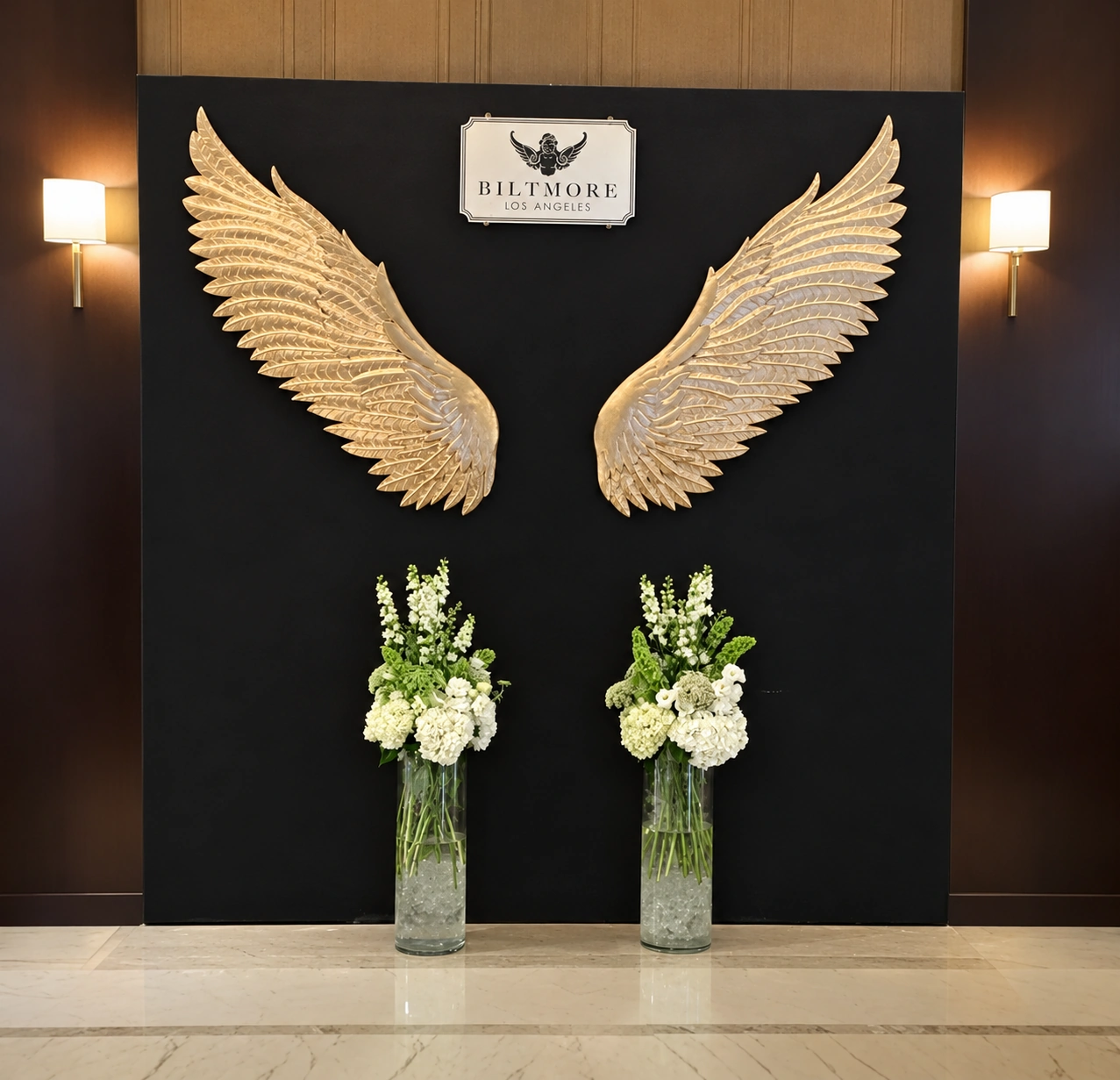 Two simple white and green floral arrangements beneath golden wings at the Biltmore Los Angeles