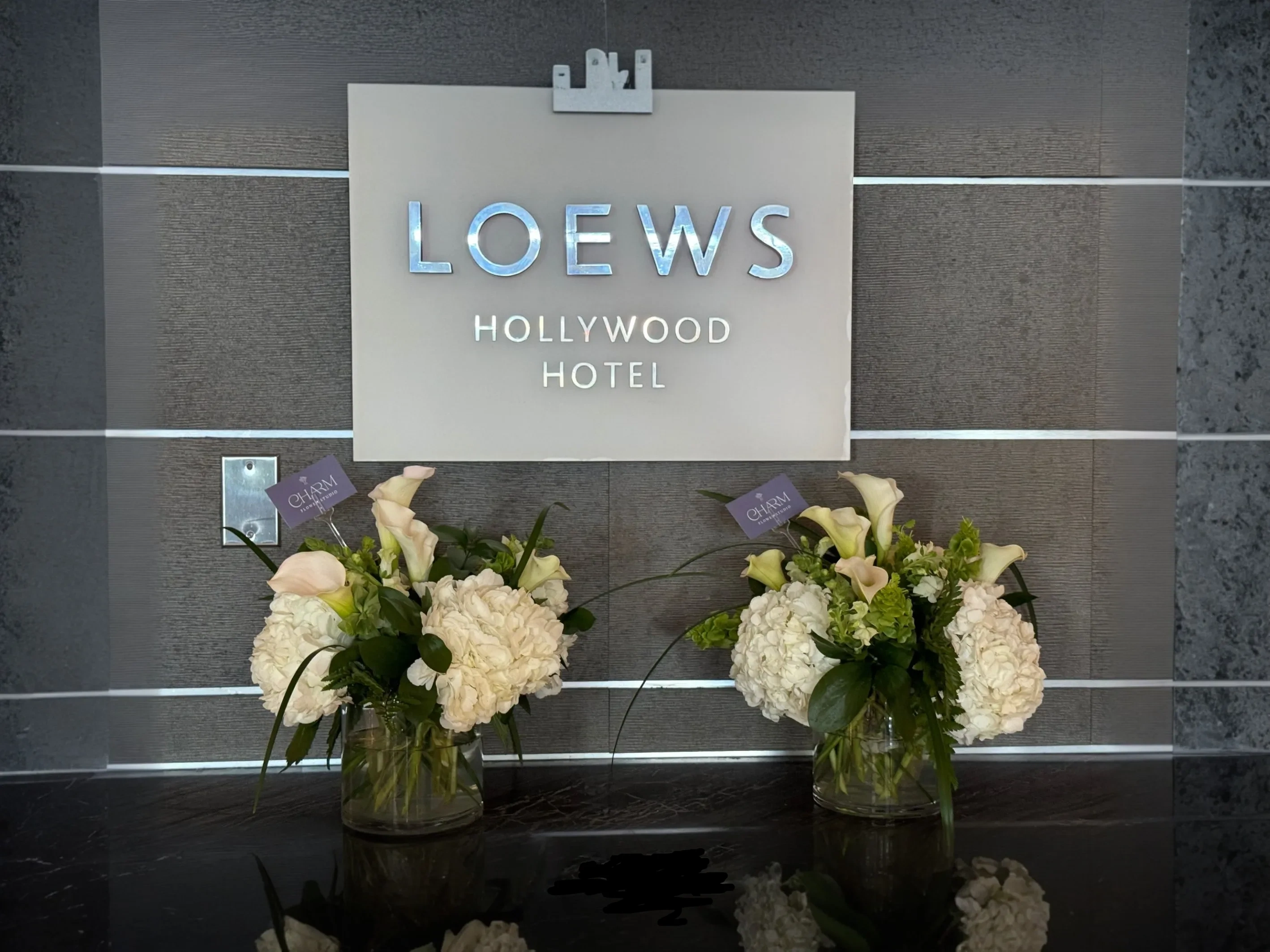 Two white hydrangea and calla lily arrangements beneath the Loews Hollywood Hotel sign