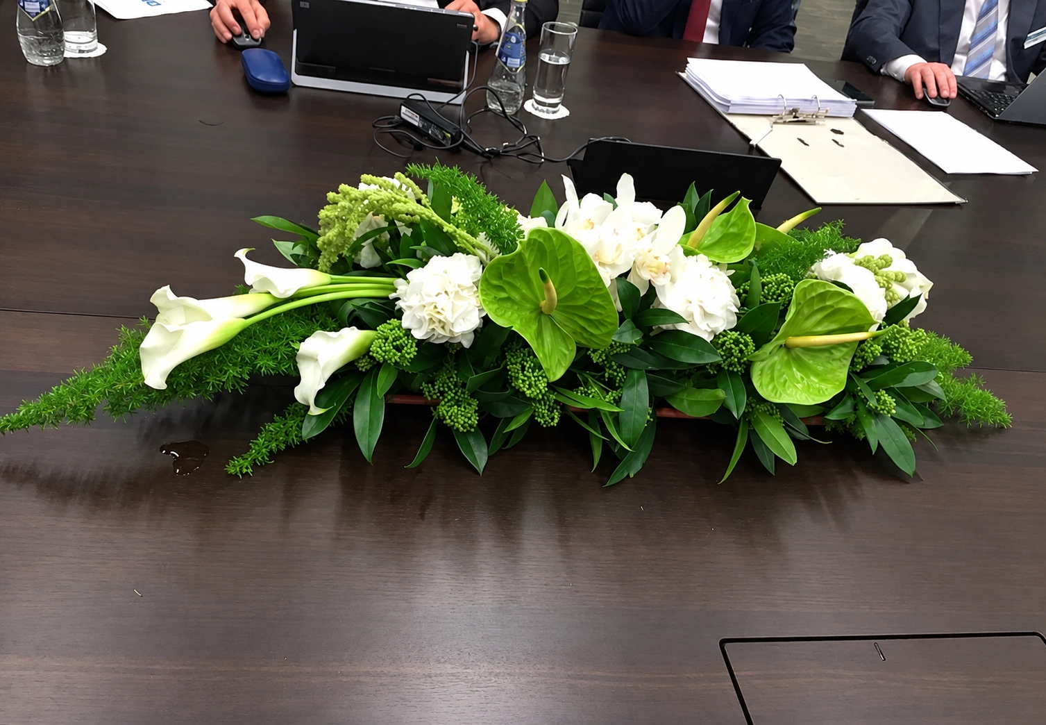 A low centerpiece with white calla lilies, hydrangeas, green anthuriums, and foliage on a meeting table
